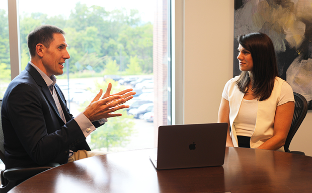Two colleagues talking in an office with a laptop on the table.