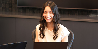 Two people sit at a table using laptops in a modern office.
