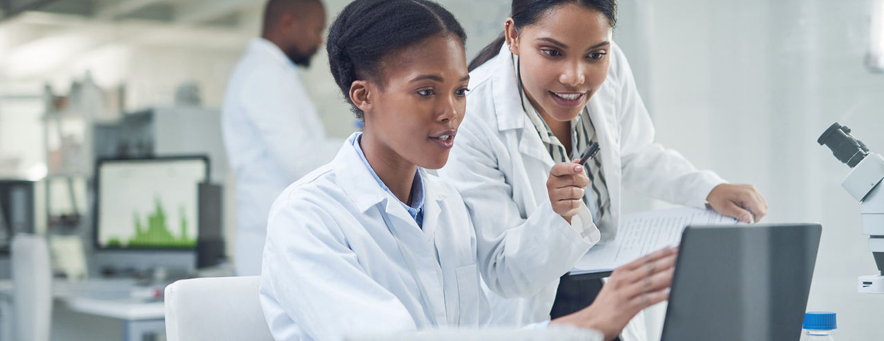 Two scientists on computer with another in the background, in a lab setting 