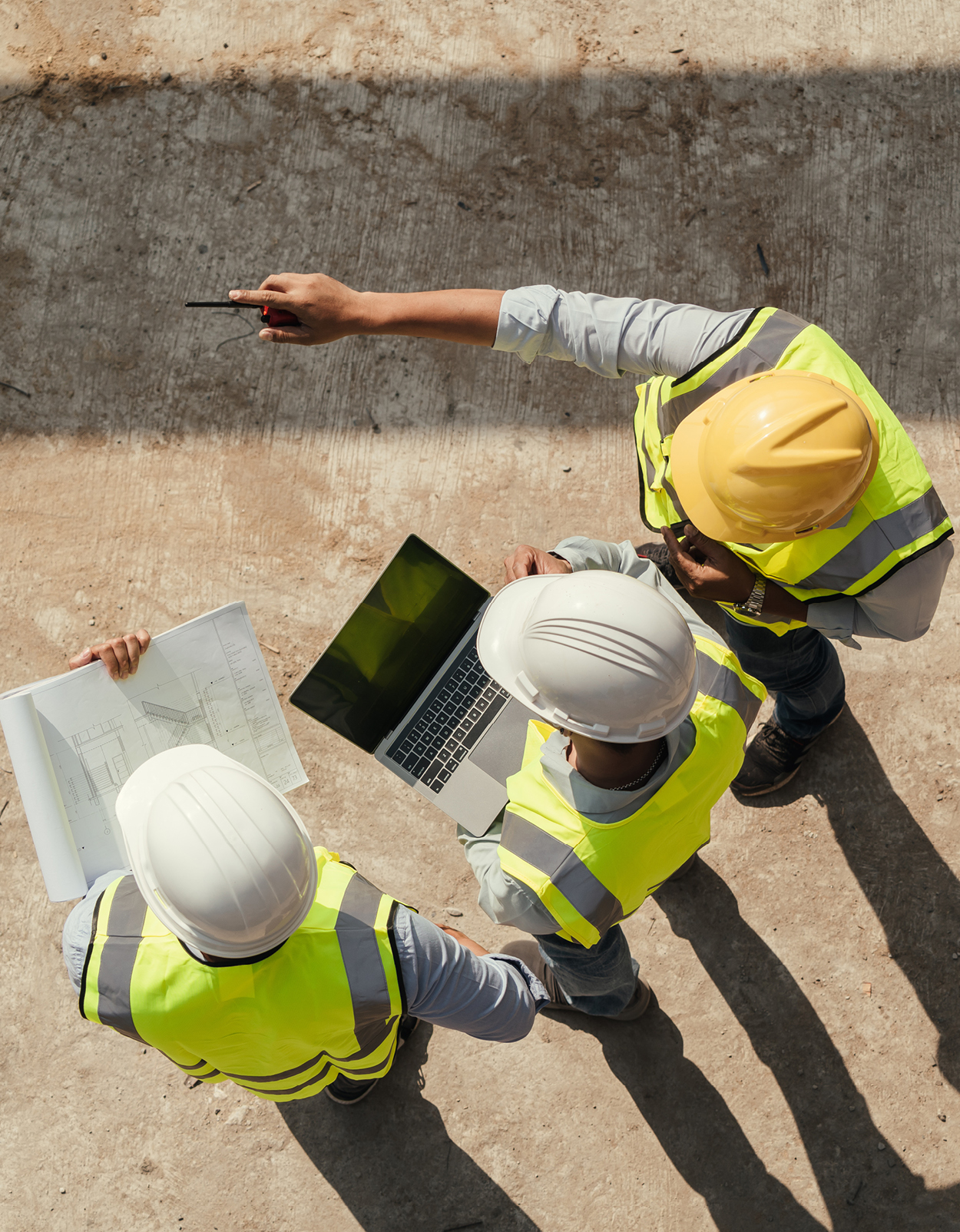 Top-down view of 3 construction workers collaborating on laptop.