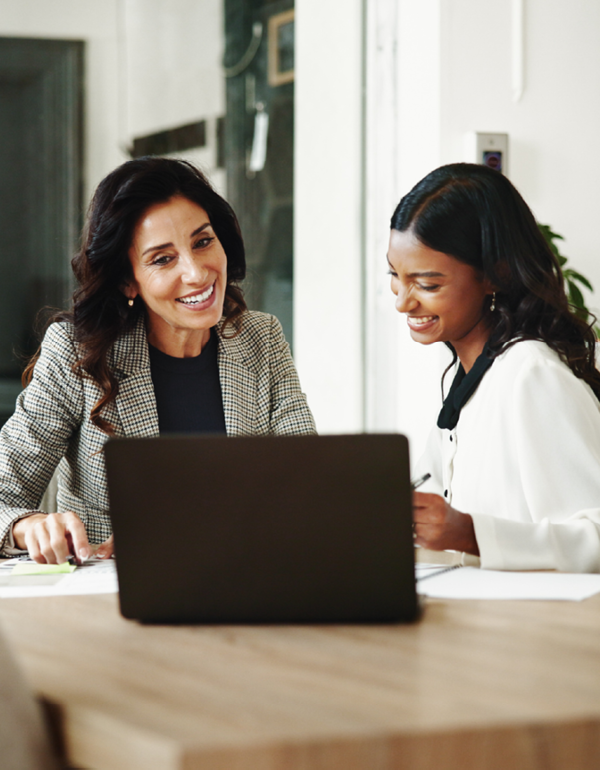 Two colleagues smiling and reviewing work on a laptop.