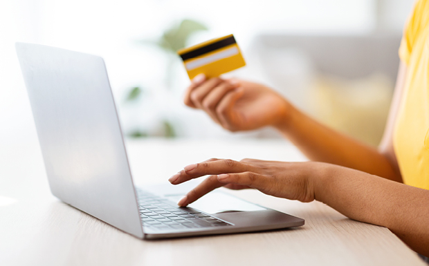 Person typing on a laptop and holding a credit card