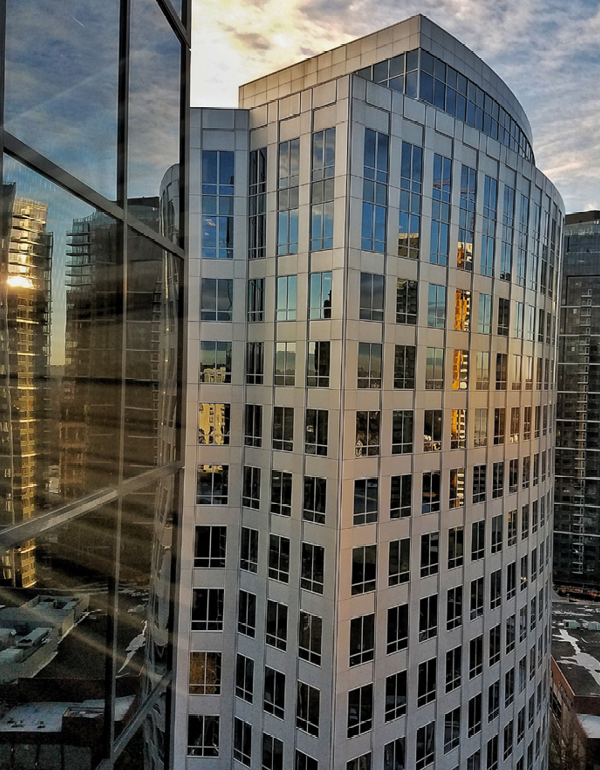 Glass office tower reflecting nearby city buildings.