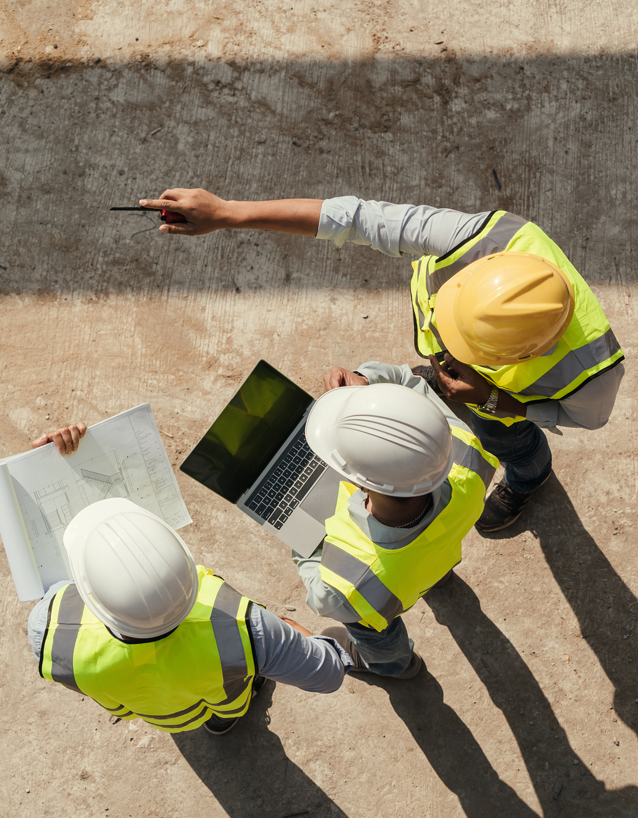 Construction workers on site with laptop and blueprint.