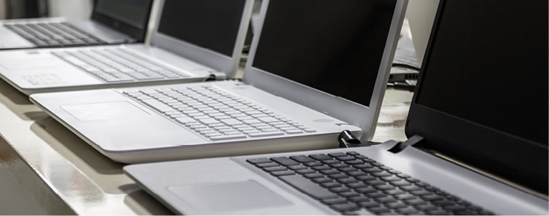 Laptops sitting on a table in a row.