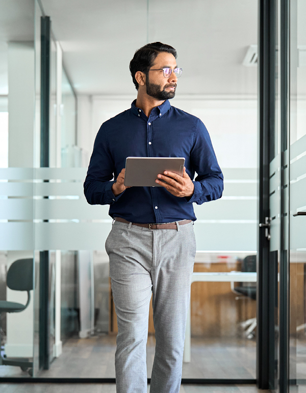 Person carrying a tablet and walking through a contemporary office corridor with glass partitions and meeting spaces.