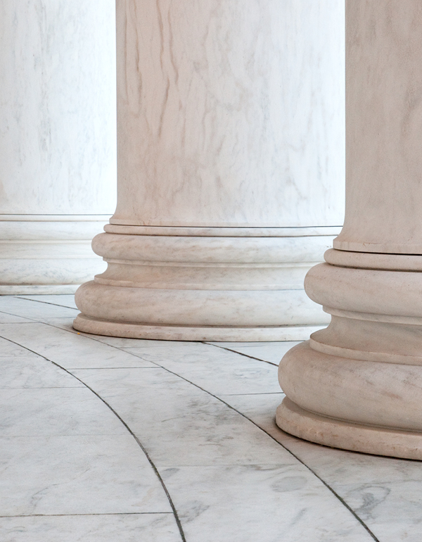 Detail of white marble columns with decorative bases standing on a curved marble floor, highlighting the symmetry and craftsmanship of a classical civic or institutional building.