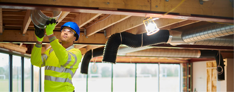 Man installing HVAC system into warehouse under construction.