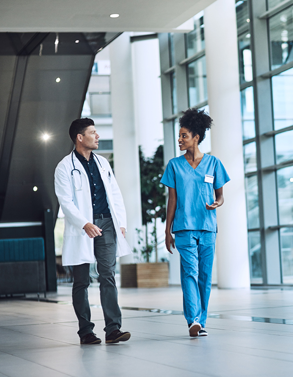 Two healthcare professionals walk together down a modern hospital hallway.