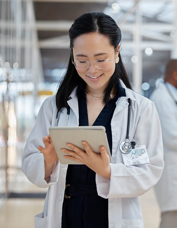 A doctor in a white lab coat reviews information on a digital tablet in a bright, modern medical facility.
