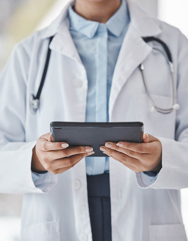 A doctor in a white lab coat holds a tablet while reviewing information.