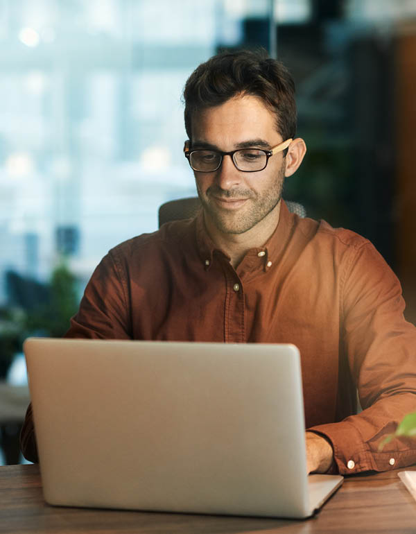 An individual works intently on a laptop at a desk in a modern office setting.