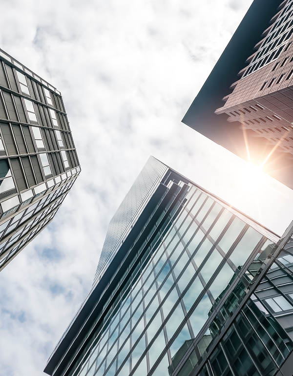 Glass skyscrapers rise into a partly cloudy sky, viewed from below.