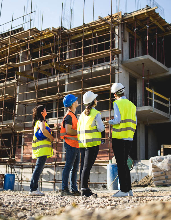 Four construction workers observe a multi-story building under construction.
