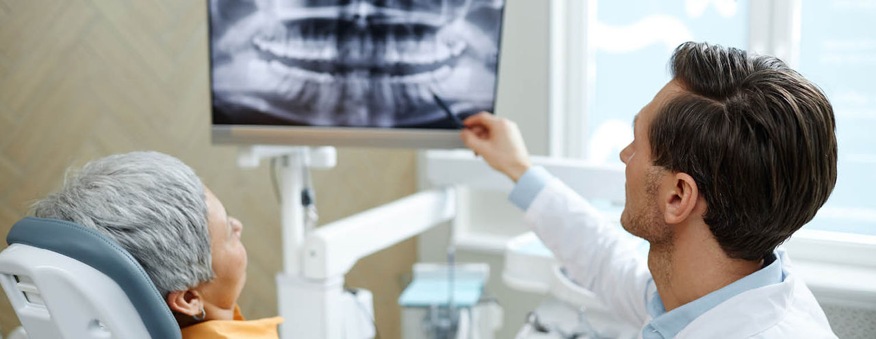 A dentist shows a patient a dental X‑ray on a monitor while discussing their treatment.
