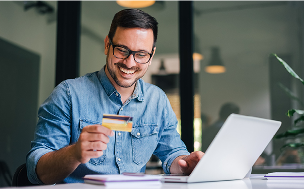 Man smiling and holding credit card and working on laptop.