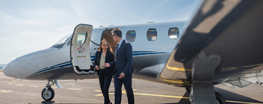 Two people standing beside a small private jet on a runway.
