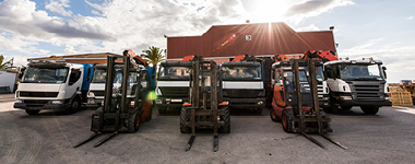 Trucks and forklifts lined up in construction company with industrial warehouse behind.