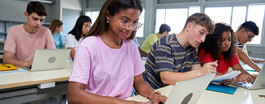 Students smiling and working on laptop in classroom
