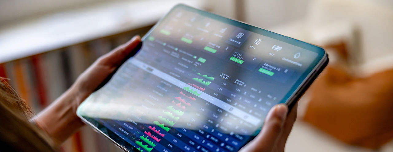 A person holds a tablet showing a stock market app with financial data.